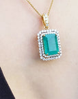 Gold necklace with a natural emerald into a double halo diamond pendant on a person's neck.