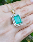 Gold necklace with a colombian emerald pendant held in a hand against a blurred green background