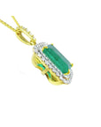 The underside profile view of a yellow gold pendant with a natural emerald and diamonds on a white background