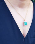 Person wearing a black sleeveless top with a gold necklace featuring an emerald pendant.