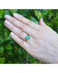 Hand wearing a 1.22 carat emerald-cut Muzo Colombian emerald solitaire ring in 14K yellow gold.
