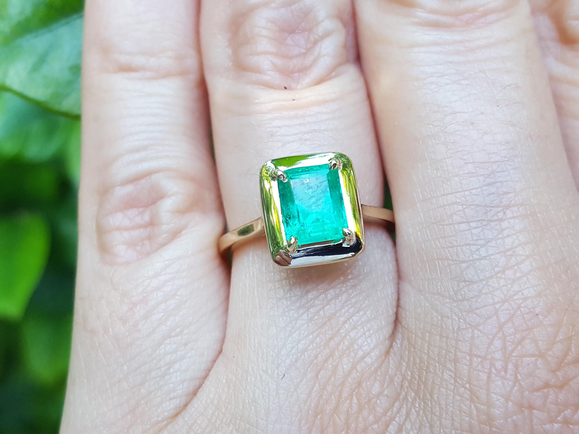 A yellow gold emerald solitaire ring on a person's finger.