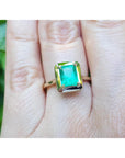 A yellow gold emerald solitaire ring on a person's finger.