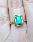 A yellow gold emerald solitaire ring on a person's finger.