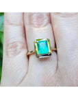 1.22 carat emerald-cut Muzo Colombian emerald solitaire ring in 14k yellow gold, worn on a hand.