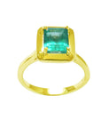 A yellow gold emerald solitaire ring displaying a rectangular emerald into a wide bezel and prong set.