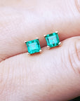 Natural emerald stud earrings on a person's finger
