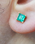 Close-up of an emerald stud earring on an earlobe.