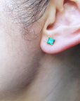 Close up of a woman's ear dressing a emerald stud earring.