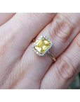Emerald-cut natural yellow sapphire halo diamond ring in 14K yellow gold on a finger.