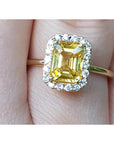 Gold ring with a yellow natural sapphire and halo diamond on a finger.
