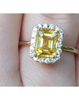 Gold ring with a yellow natural sapphire and halo diamond on a finger.