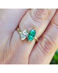 A toi et moi emerald and diamond ring marquise-cut you and me style made of 18k gold, shown worn on a person's finger.