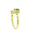 A yellow gold toi et moi emerald and diamond ring in a prong setting, with a small clear accent stone on each side.
