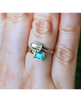 A gold you and me ring with a rectangular natural colombian emerald, shown worn on a person's finger.