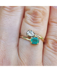 A 18k yellow gold you and me emerald and diamond ring, worn on a finger.