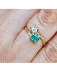 A close-up of a gold you and me ring with a square emerald-cut emerald and a smaller diamond, worn on a finger.