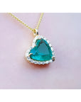 Tilted heart Colombian emerald necklace with halo diamonds on an 18K yellow gold chain.
