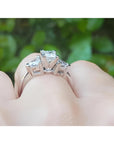14K white gold ring with a princess cut diamond center and trillion side diamonds, worn on a finger.