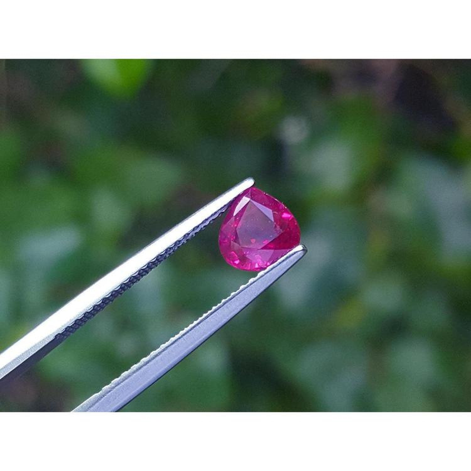 1.19 carat pear cut natural ruby gemstone, sparkling medium deep red, held in tweezers.
