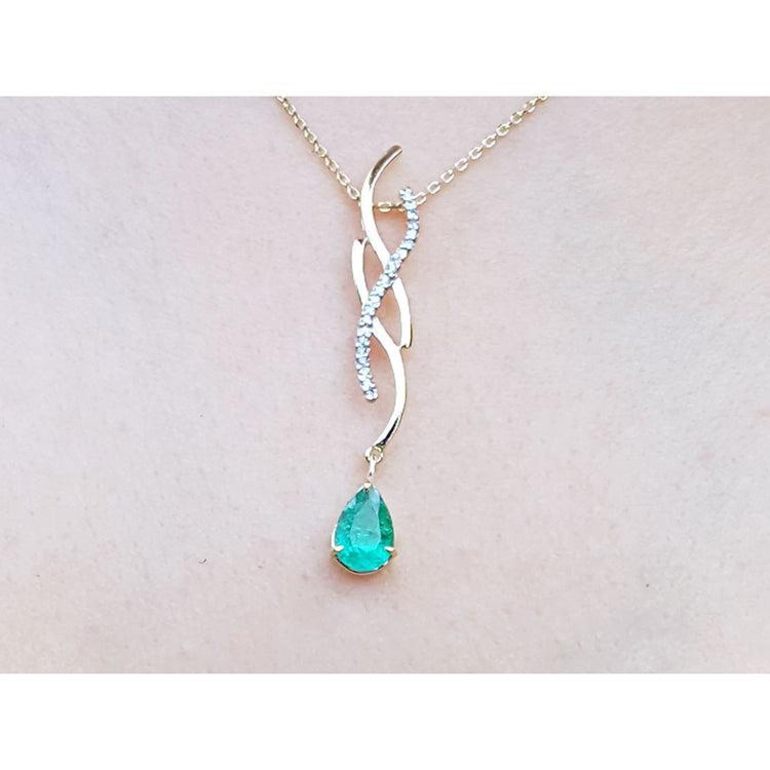 14K yellow gold twisted slider necklace with a pear-shaped emerald and diamond accents, shown worn on a person's neck.