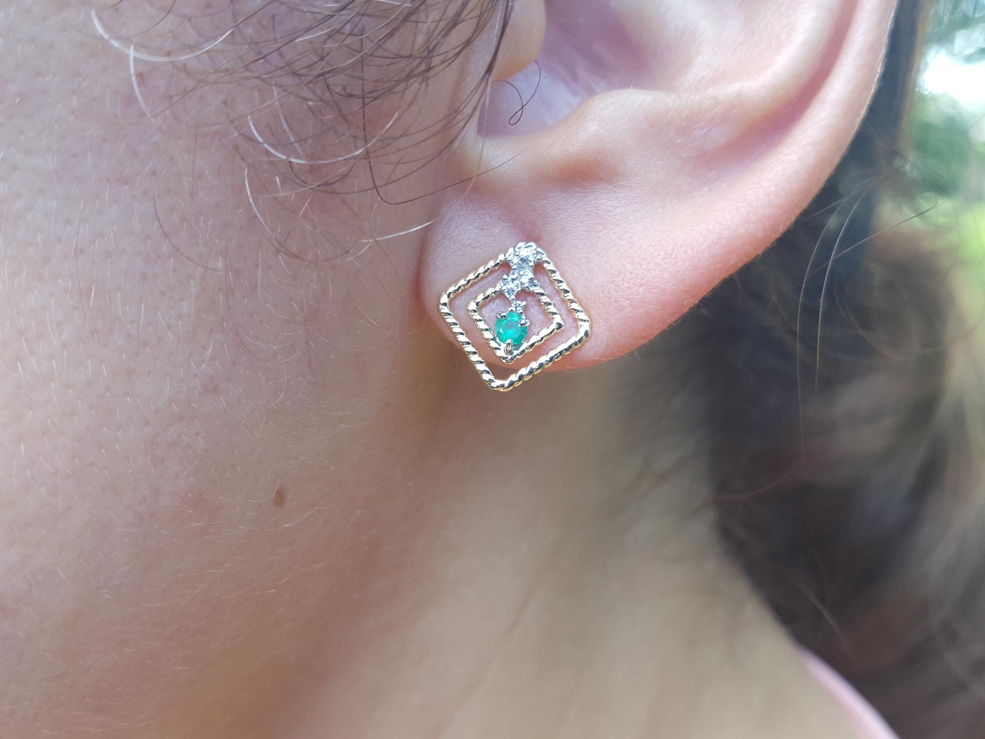 close up of a 14K yellow gold emerald post earring with round cut Colombian emerald set in a double frame rope decoration.