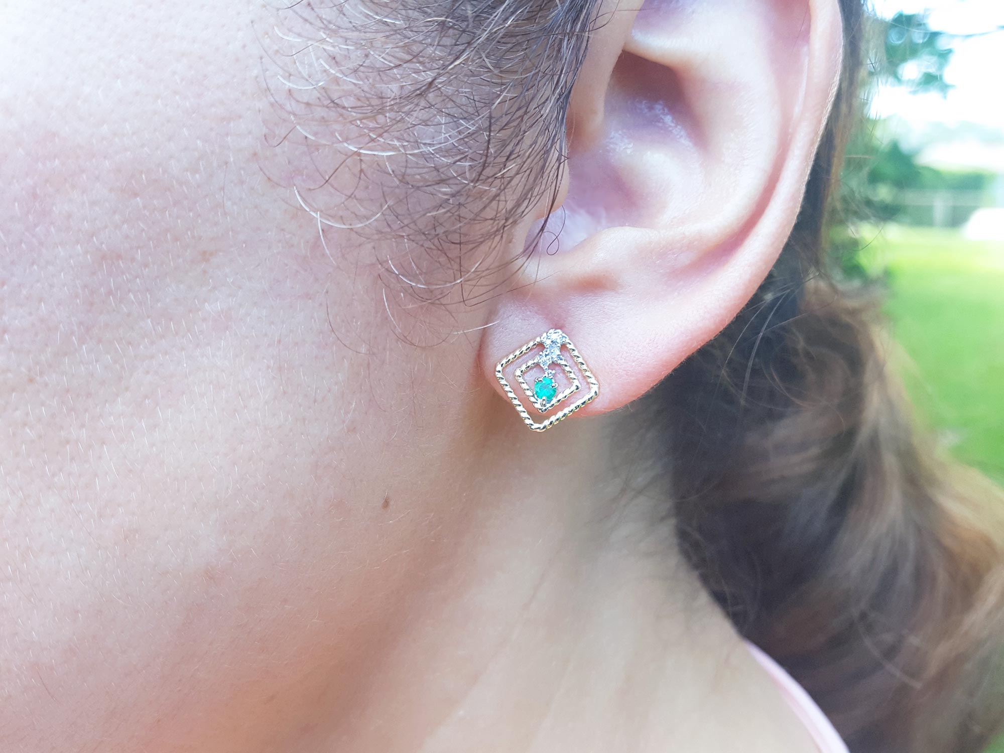 An ear wearing an earring of 14K yellow gold emerald post earring with round cut Colombian emerald.