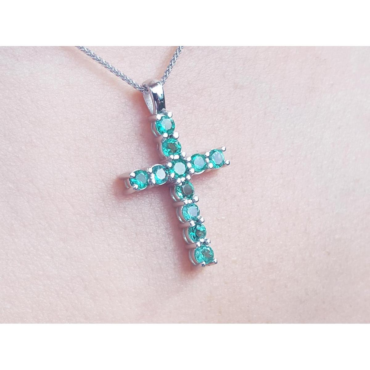 White gold emerald cross necklace on a light pink skin background.