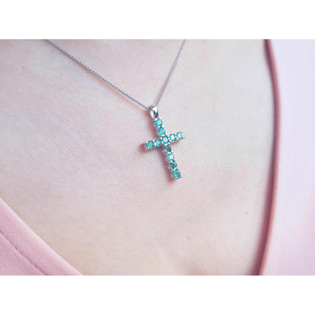 A 18k white gold emerald cross pendant necklace on a person's neck.