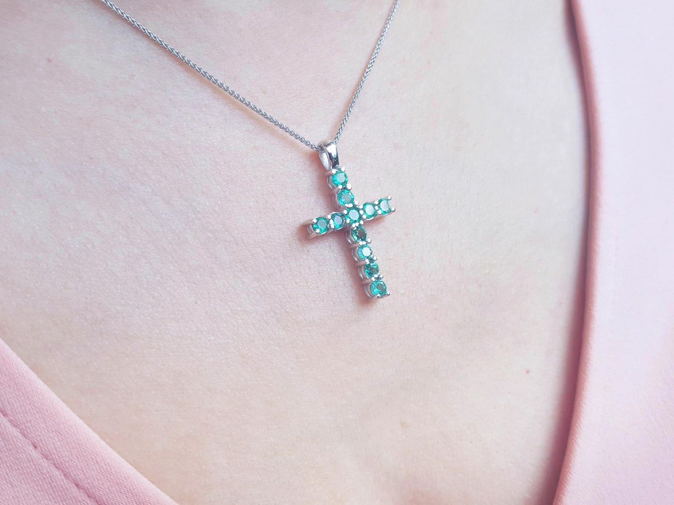A 18k white gold emerald cross pendant necklace on a person&#39;s neck.