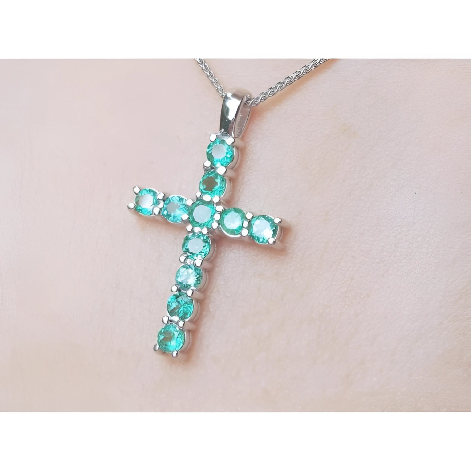Cross-shaped Muzo emeralds cross pendant on a chain against a light skin background.