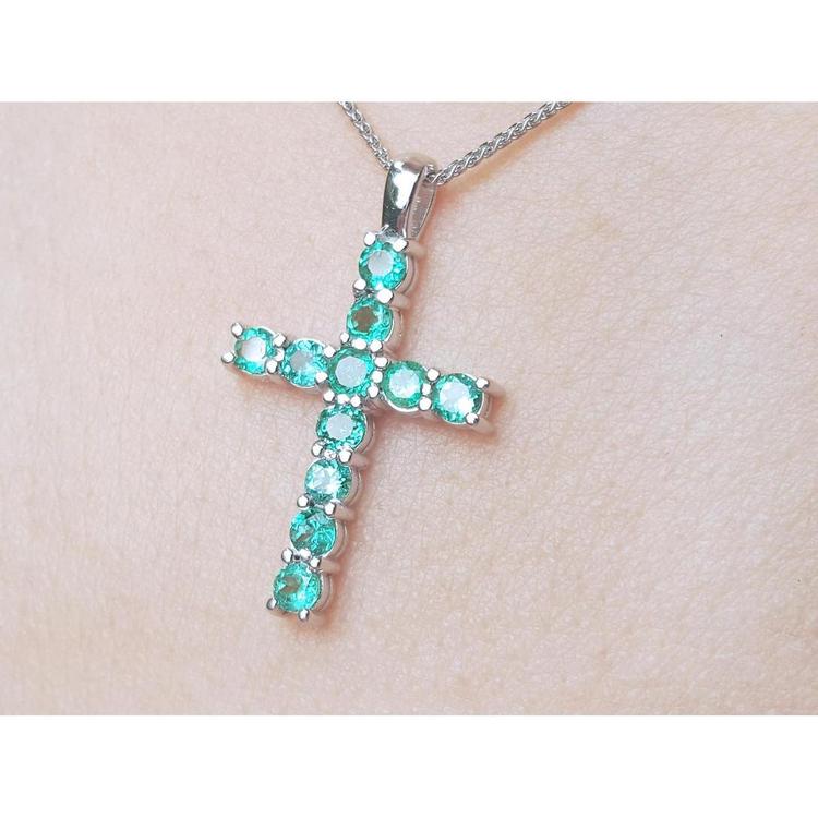 Cross-shaped Muzo emeralds cross pendant on a chain against a light skin background.