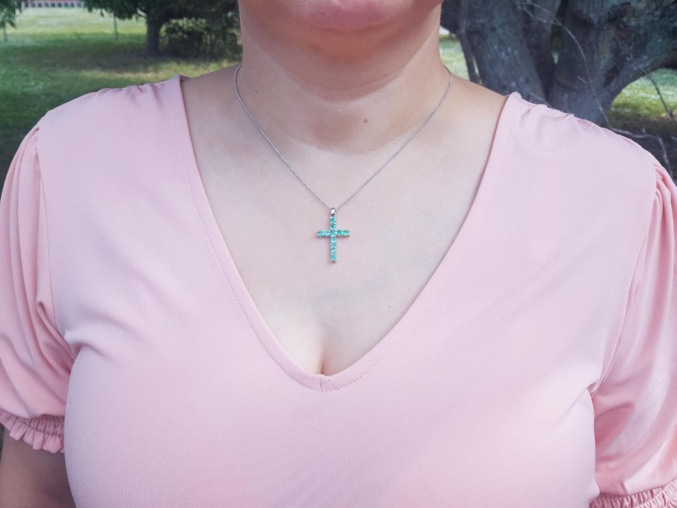 A woman wearing a pink top with a natural emerald cross necklace pendant.