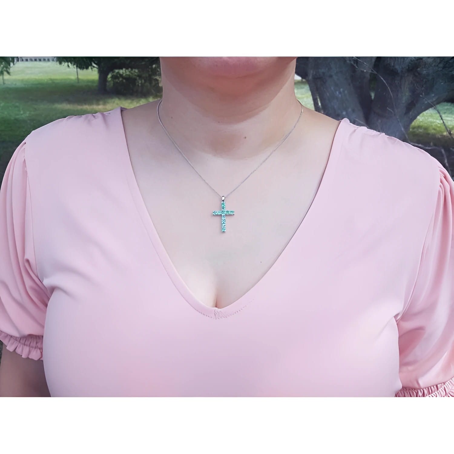 Woman wearing an 18K white gold cross pendant necklace with eleven round-cut Colombian emeralds.