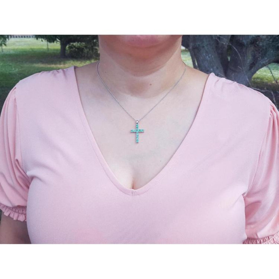 Woman wearing an 18K white gold cross pendant necklace with eleven round-cut Colombian emeralds.