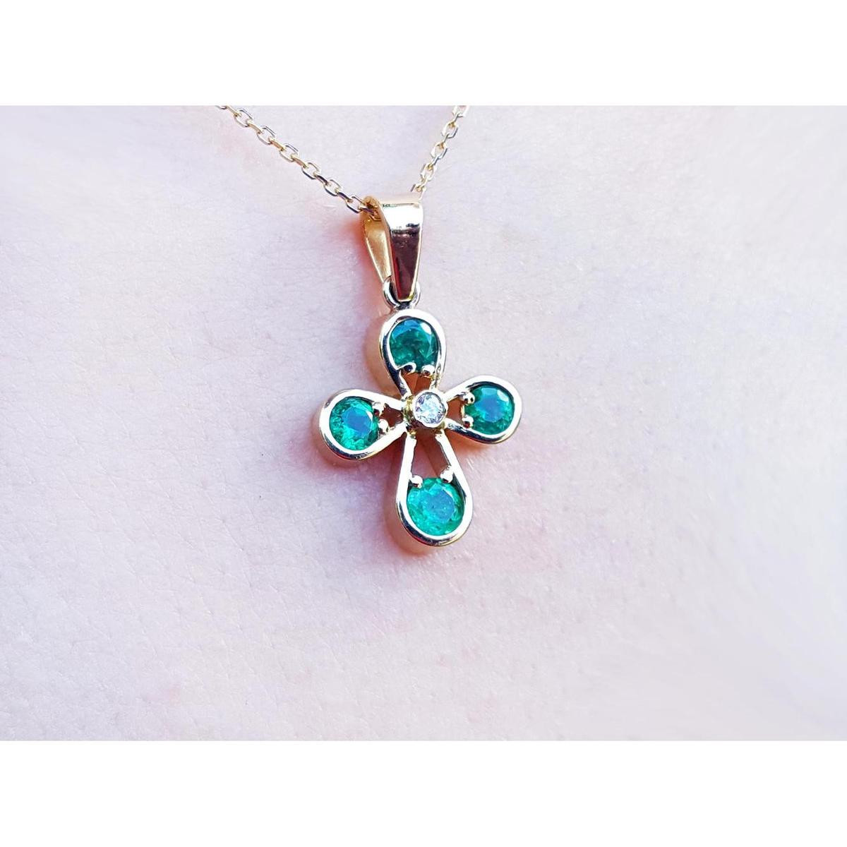 Muzo emerald cross pendant necklace on a light pink skin background.