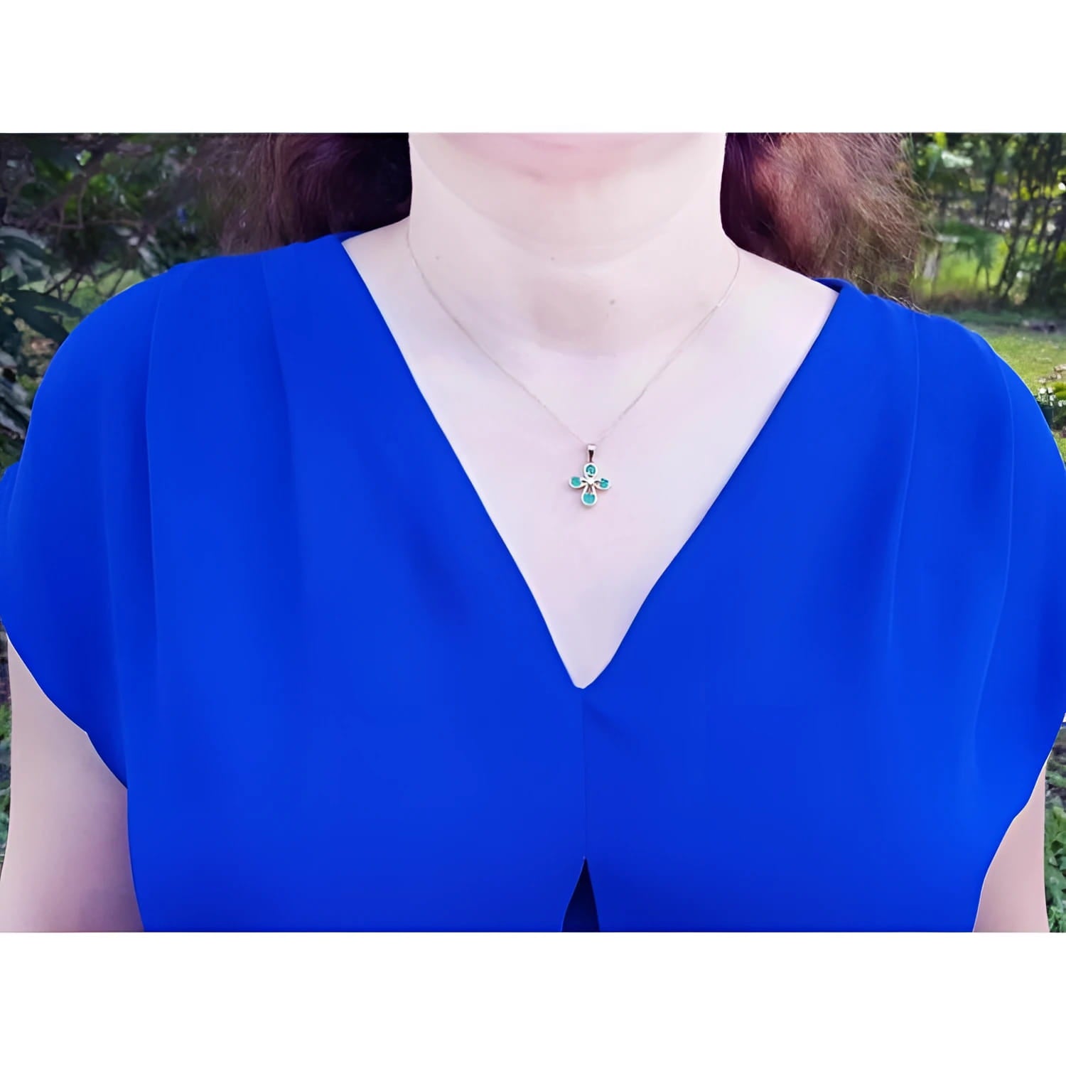 Yellow gold cross pendant with round-cut emeralds on a woman's neck, wearing a blue top.