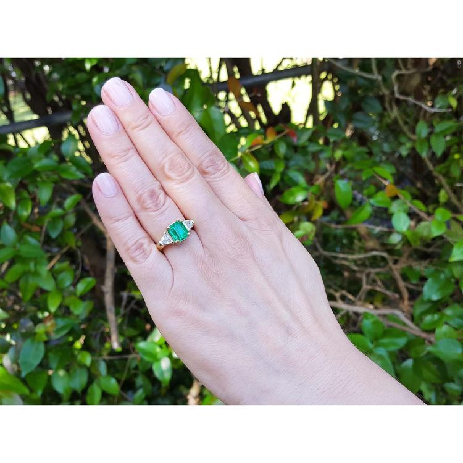 18K yellow gold ring with a GIA certified emerald and side trillion diamonds on a hand.