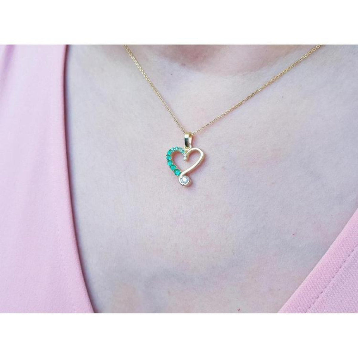 18K yellow gold heart pendant with natural emeralds and a diamond, worn on a woman's neck.