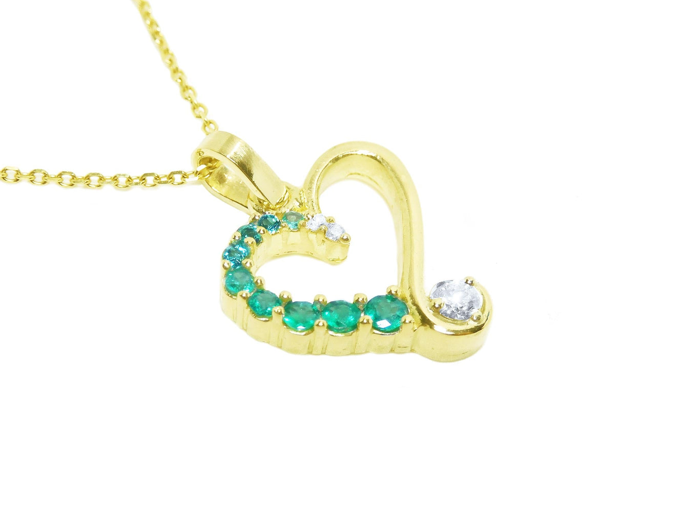 Gold heart-shaped pendant with natural emeralds and diamond on a topside view position.
