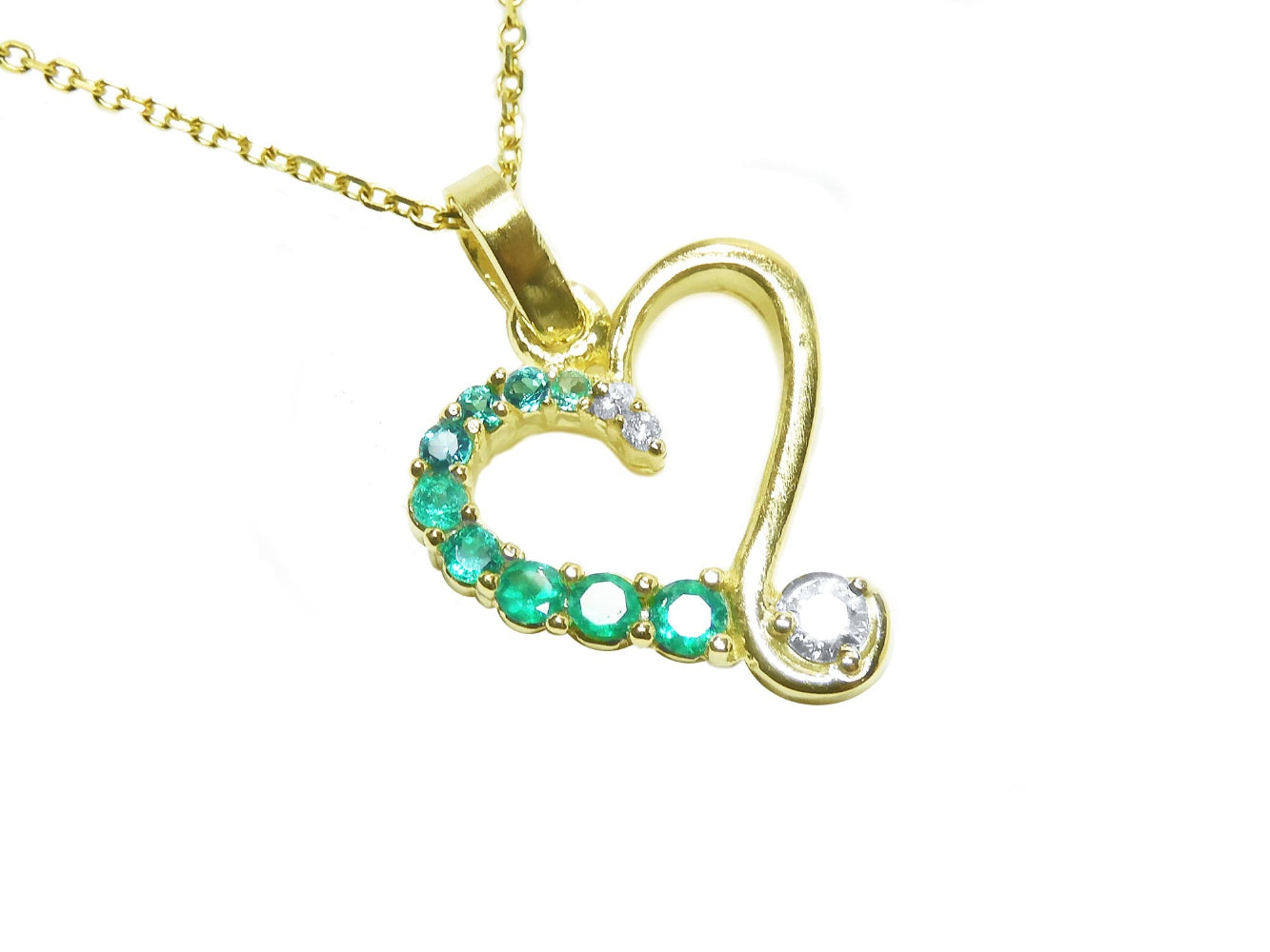 Gold heart-shaped pendant with round cut emeralds gemstones on a white background.