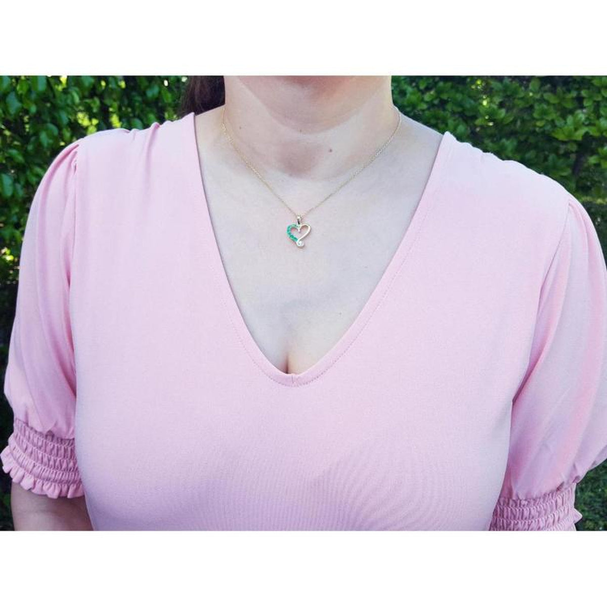 Emerald and diamond heart pendant in 18K yellow gold on a woman's neck.