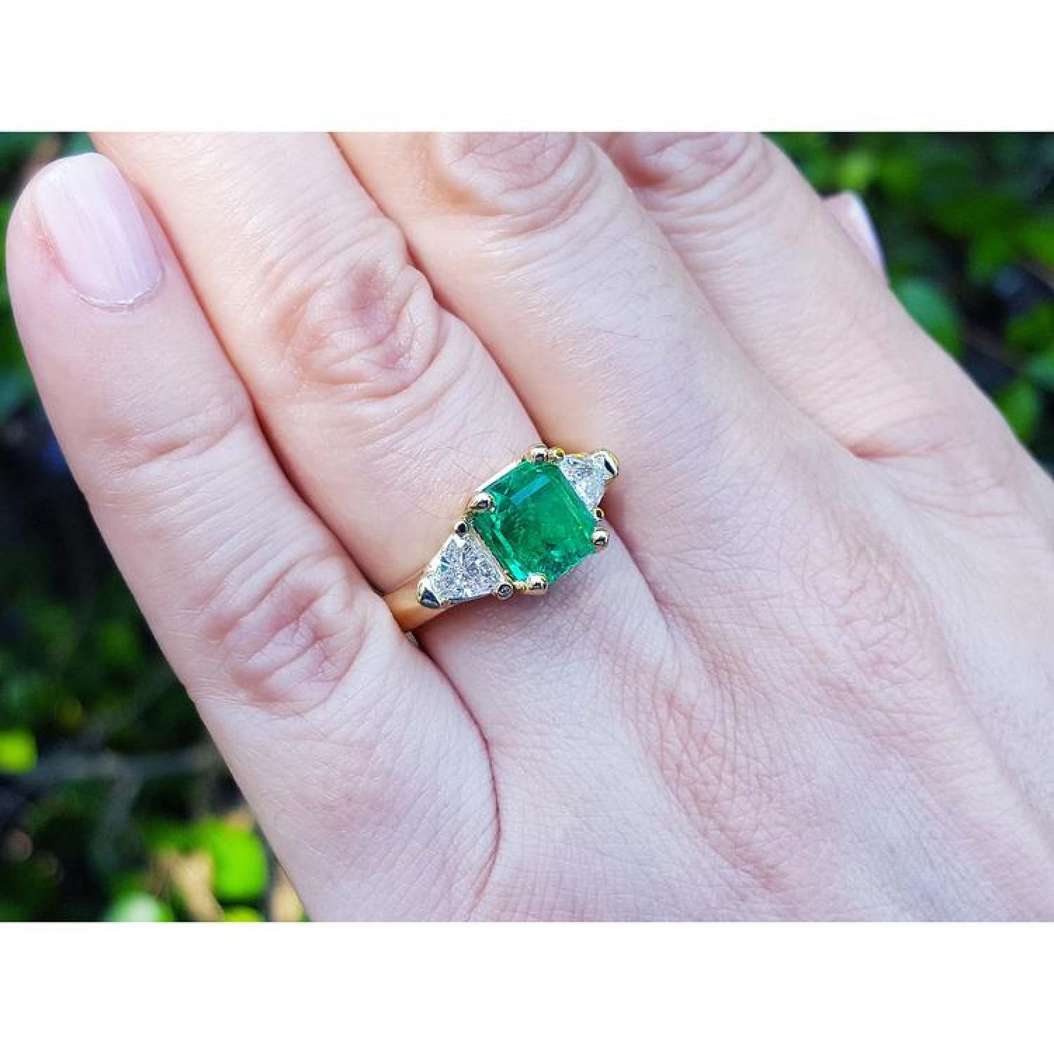 18K yellow gold ring with a GIA certified emerald and side trillion diamonds on a hand.