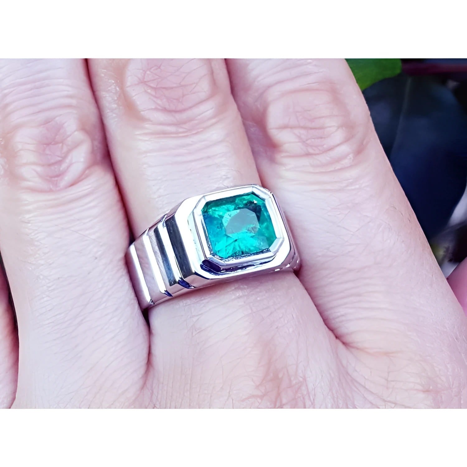 A 18k white gold men's ring with a bezel set natural colombian emerald worn on a finger.