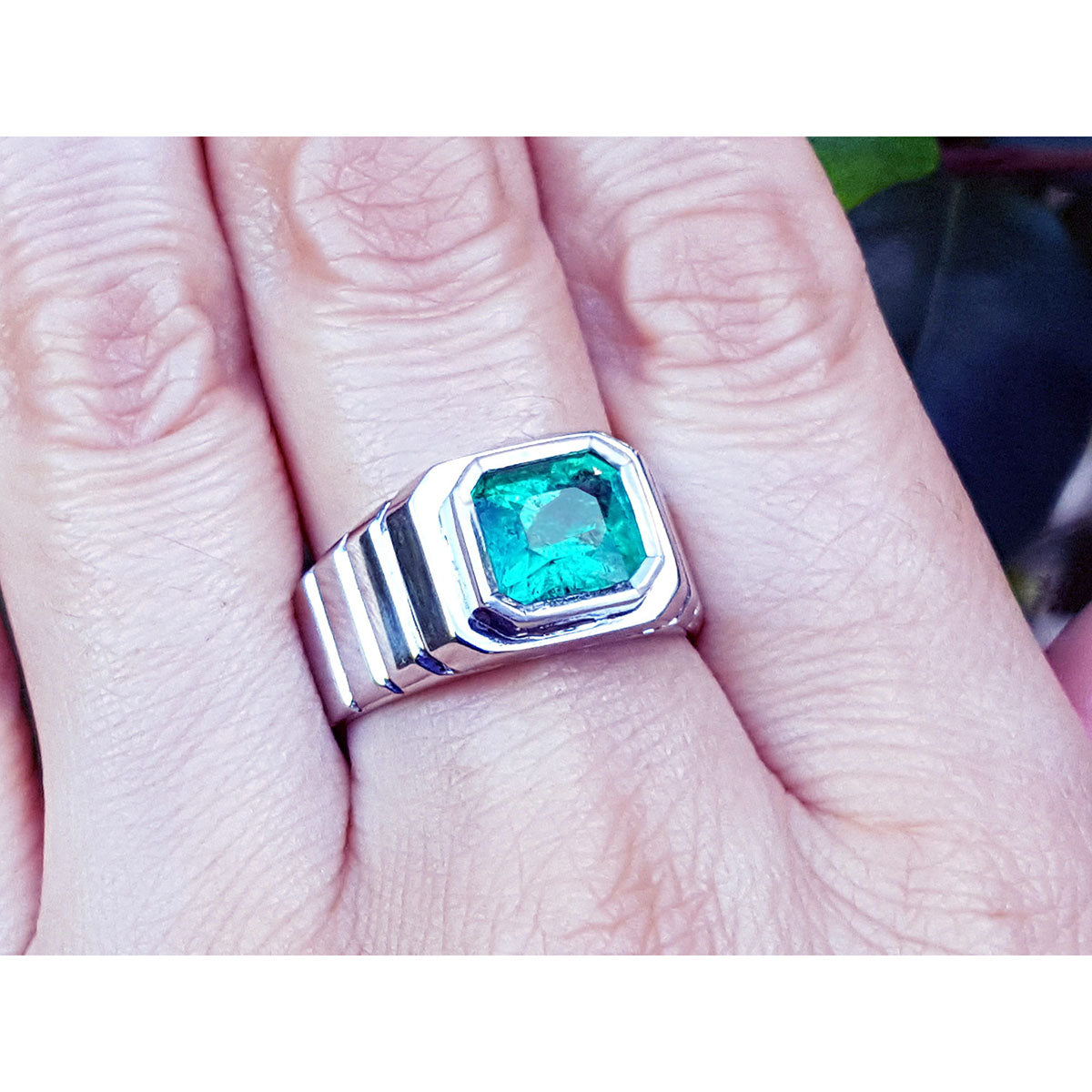 A white gold men's ring with a bezel set natural colombian emerald on a finger.