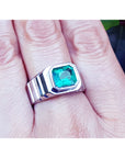 A white gold men's ring with a bezel set natural colombian emerald on a finger.