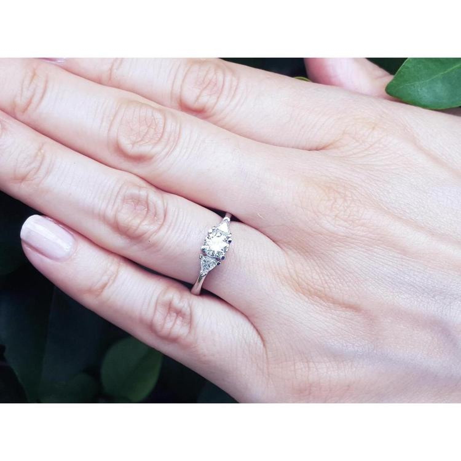 14K white gold engagement ring with a round center diamond and trillion side diamonds on a hand.
