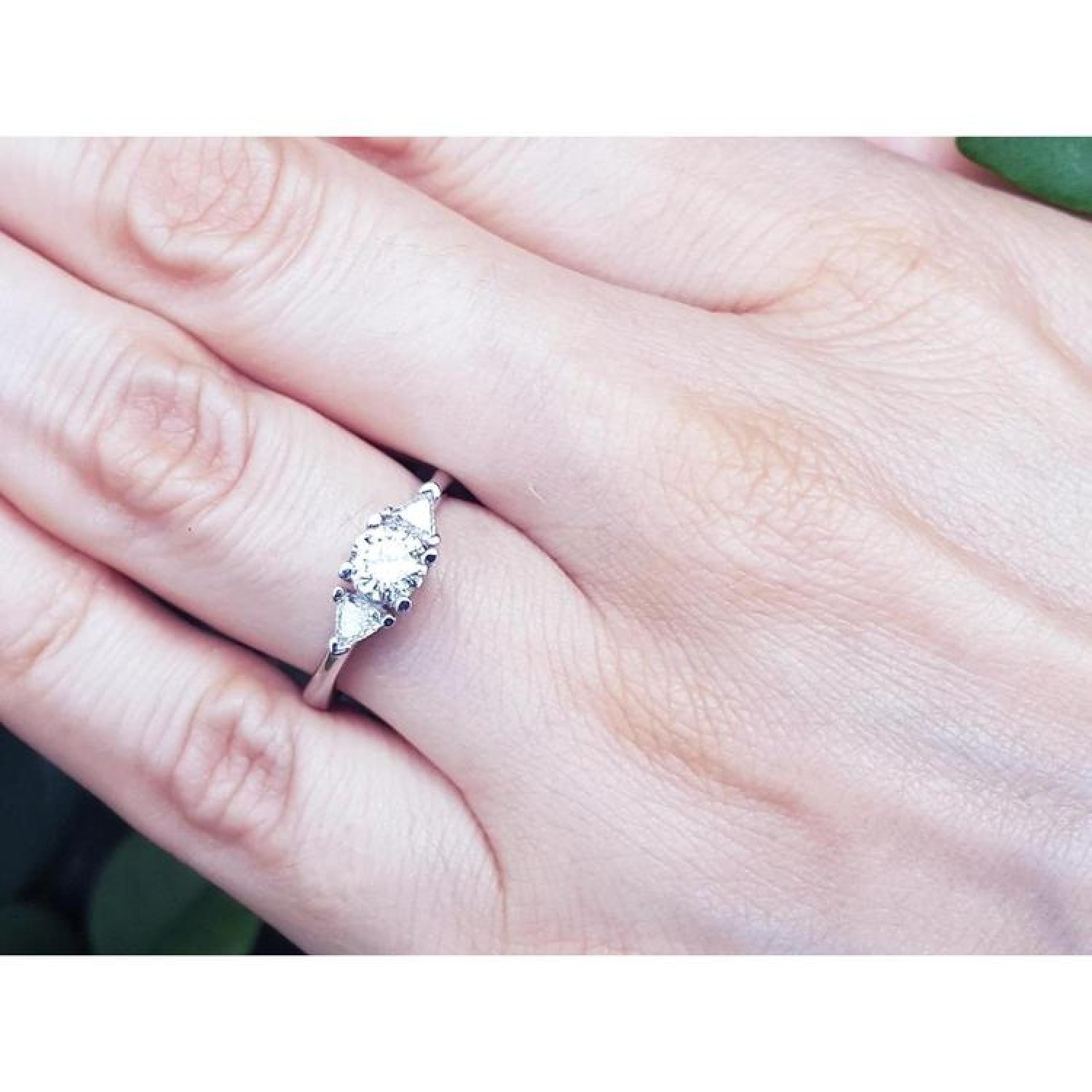 14K white gold engagement ring with a round center diamond and two trillion side diamonds on a hand.