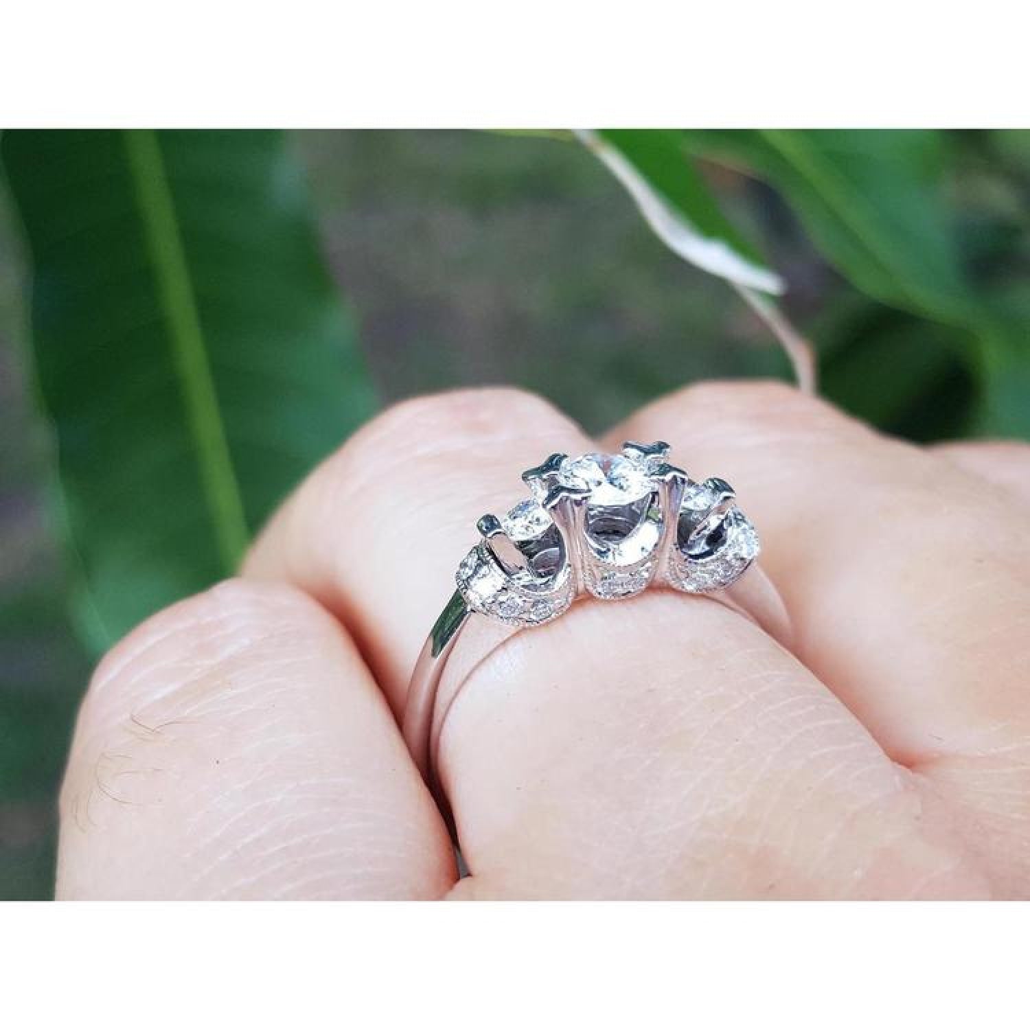 14K white gold three-stone round cut diamond engagement ring with pave set accent diamonds.