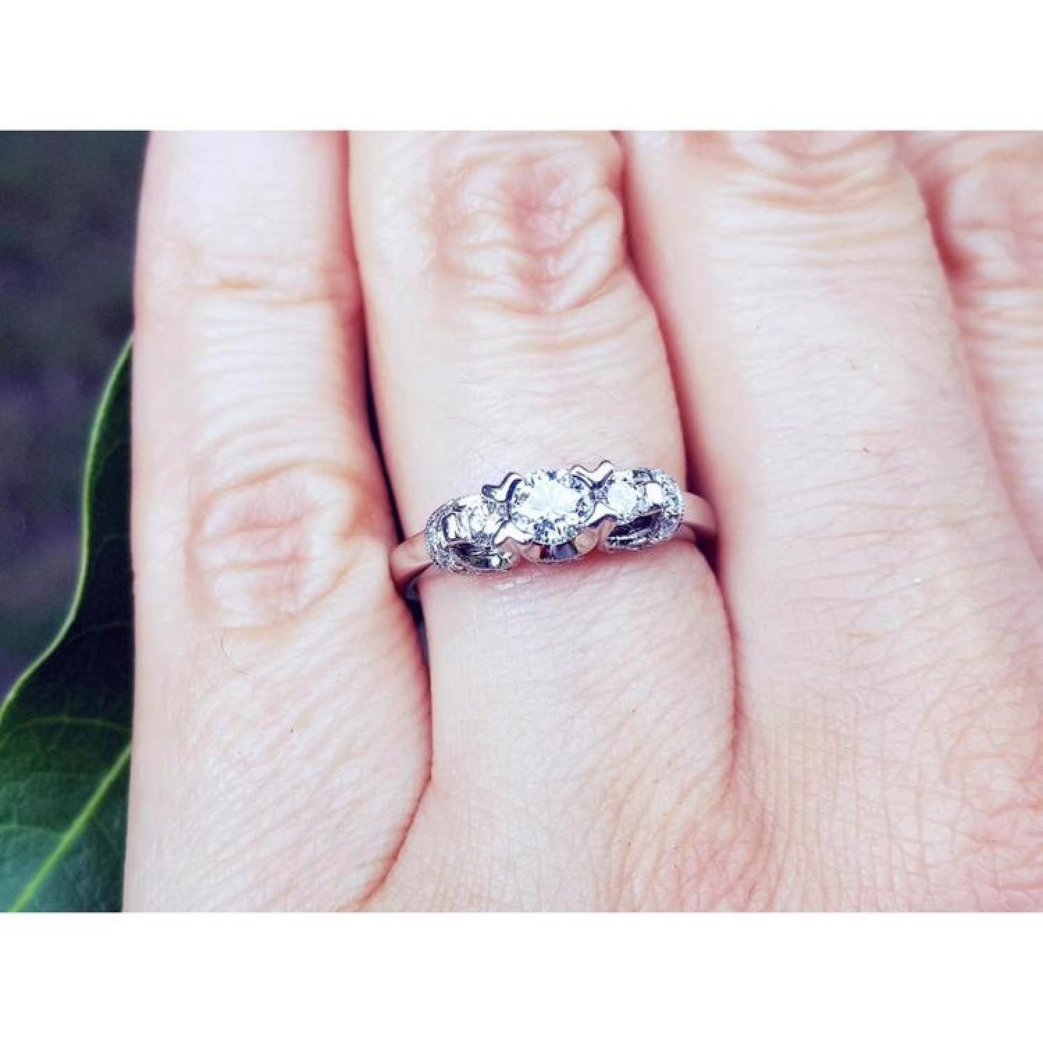 14K white gold three-stone round cut diamond engagement ring with pave accent diamonds on a hand.